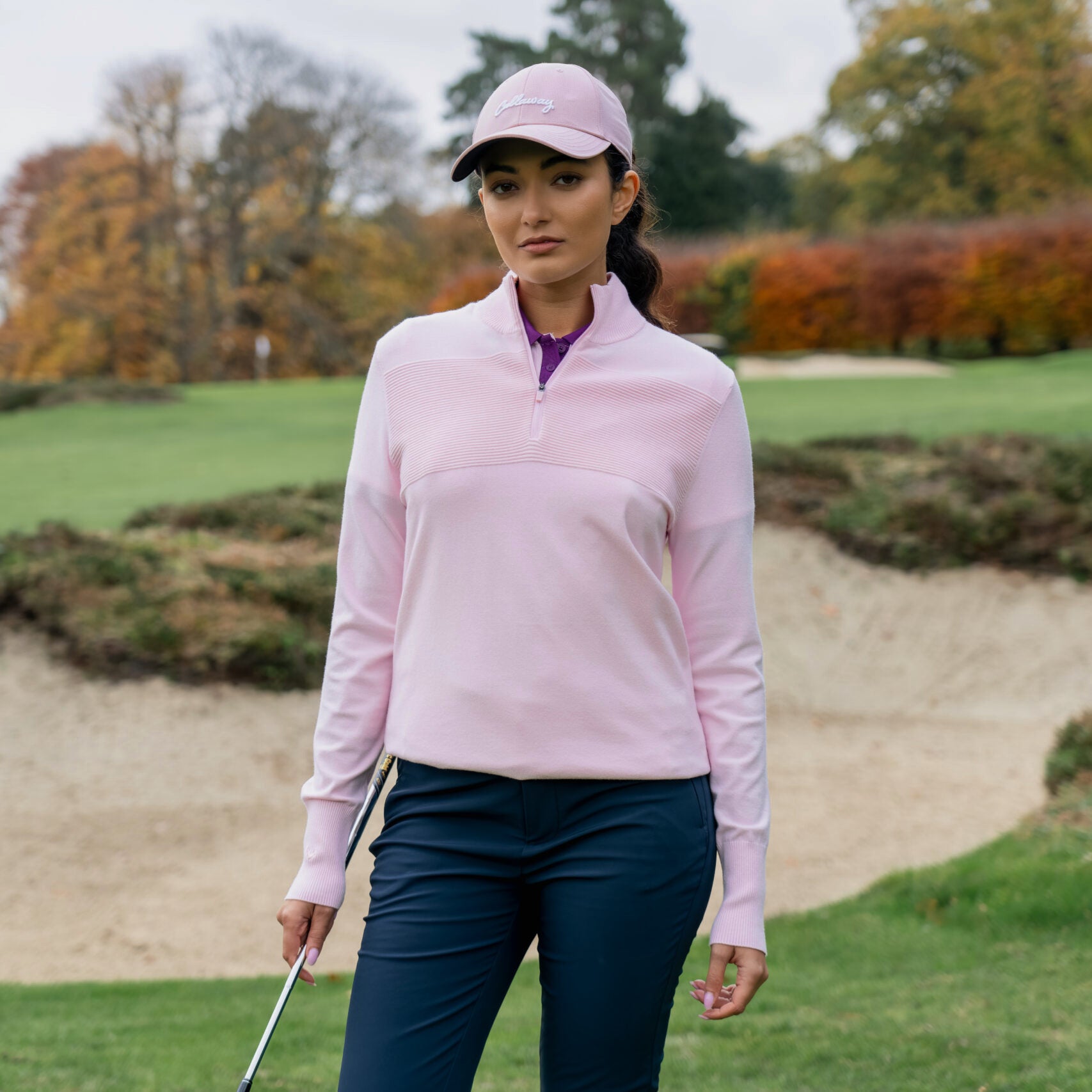 Golfistka v svetru Callaway Soft Stretch Zip-Neck v barvě třešňového květu na golfovém hřišti