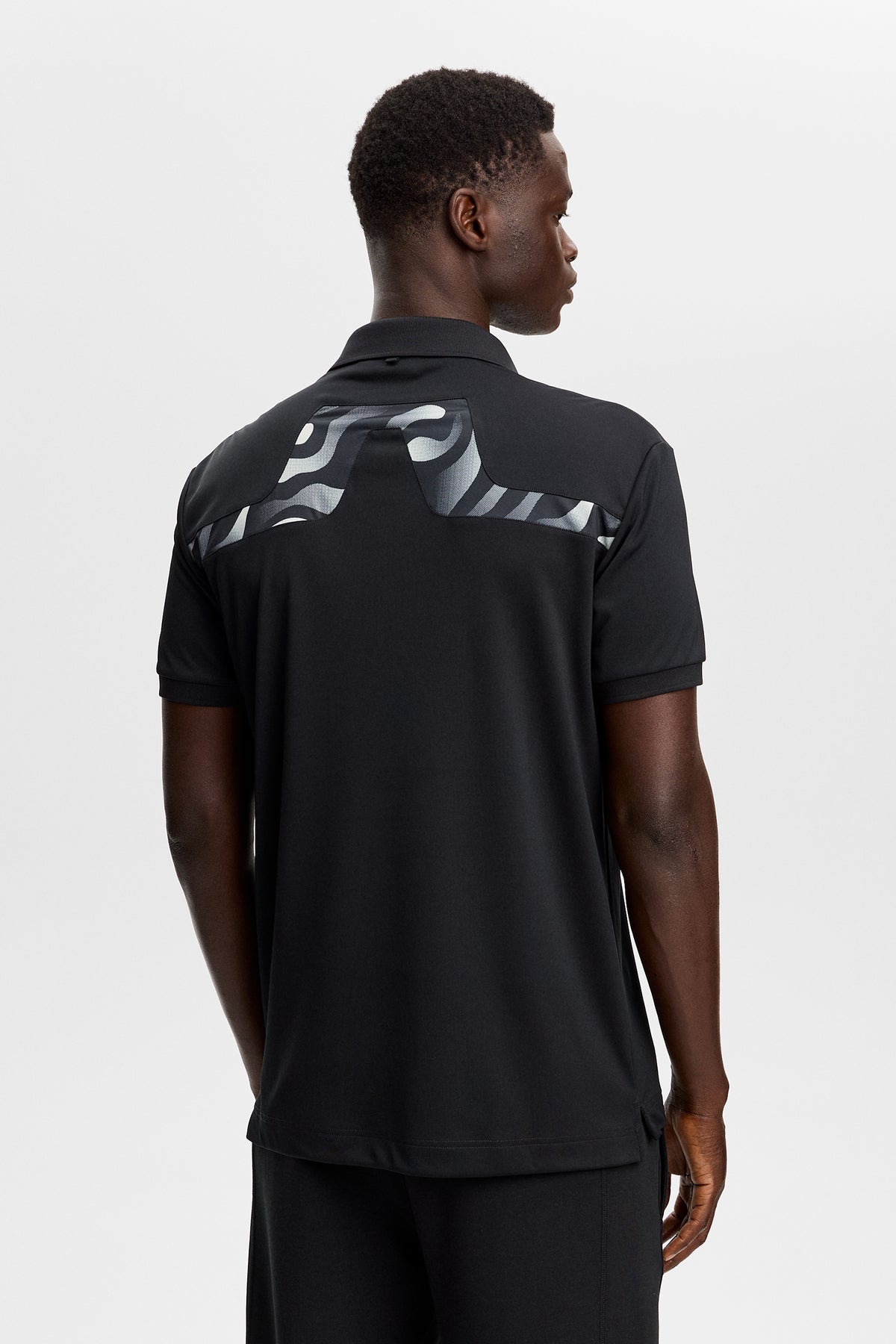 J.Lindeberg KV Print Polo Black – lifestylová fotografie na hřišti demonstrující ochranu proti slunci UPF 40+